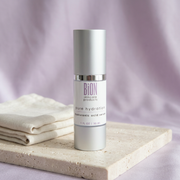 BiON Pure Hydration Hyaluronic Serum silver bottle on pale stone beside ivory linen with soft lilac background