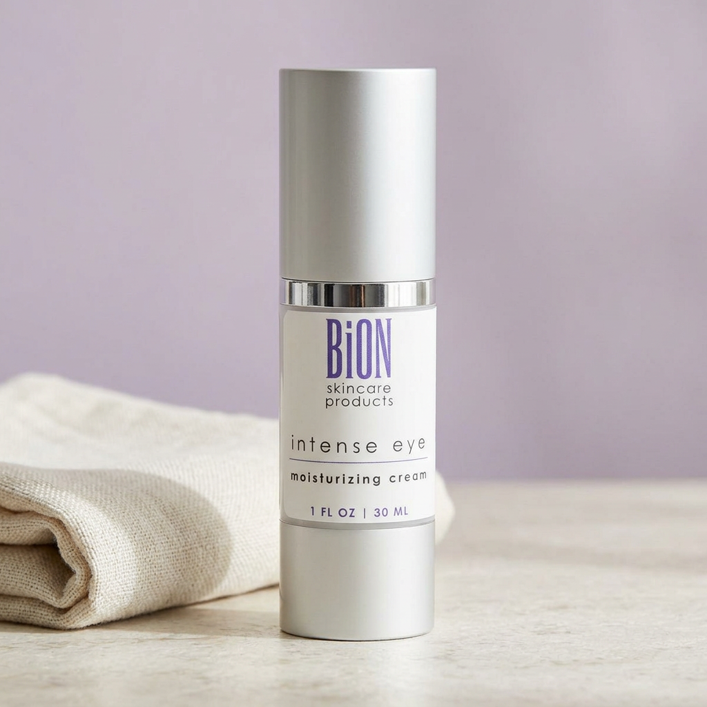 BiON Intense Eye Moisturizer silver bottle on pale stone beside folded ivory linen and a lilac backdrop