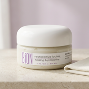 BiON Restorative Balm jar on pale stone beside ivory linen with soft lilac background